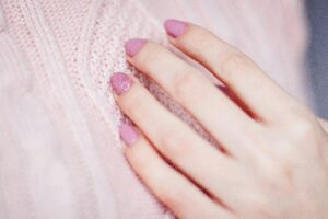 Close-up of a woman's hand with pink manicure resting on a soft knit sweater, showcasing elegance and fashion.